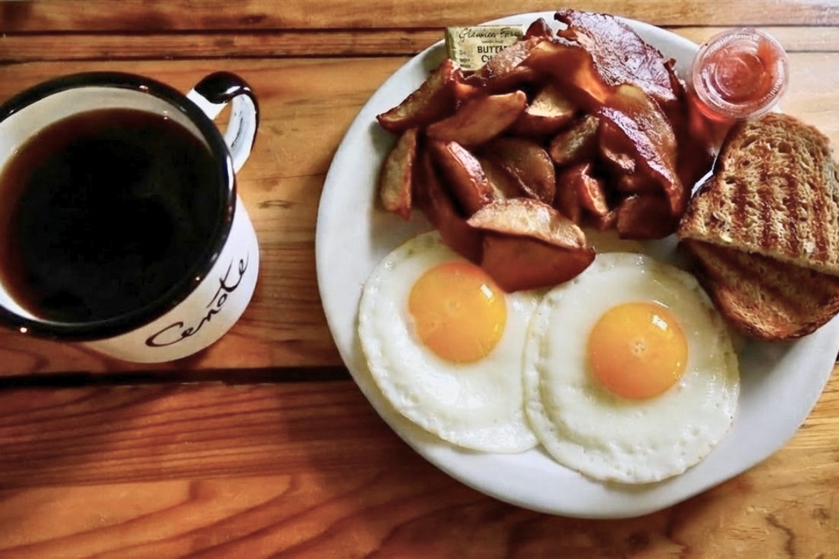 Cenote branded coffee mug with classic American breakfast plate of sunny-side up eggs, home fries, bacon and toast at Cenote cafe on East 7th St in East Austin