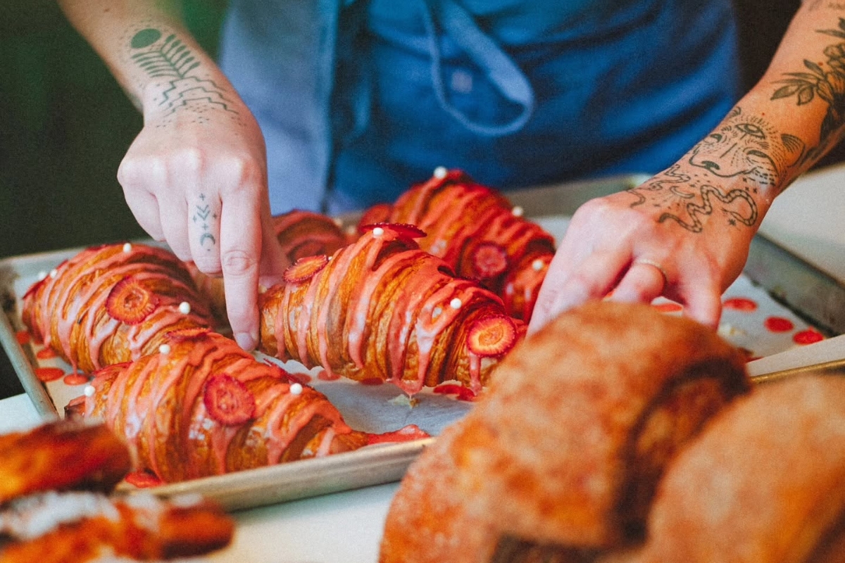 Baker arranging freshly made strawberry-glazed croissants on a baking sheet at Rockman Coffee and Bakeshop on East Cesar Chavez St in East Austin