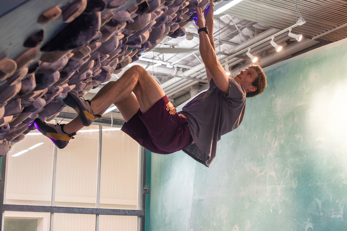 A climber tackling a steeply overhanging bouldering wall at Austin Bouldering Project's Springdale location, one of the best active things to do indoors in Austin near the Heywood Hotel.